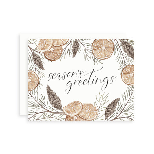 Greeting card with 'season's greetings' text surrounded by watercolor illustrations of orange slices, pine branches and pinecones.
